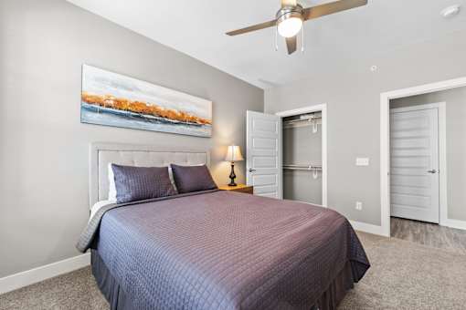 A bedroom with a bed, a ceiling fan, and a painting on the wall.