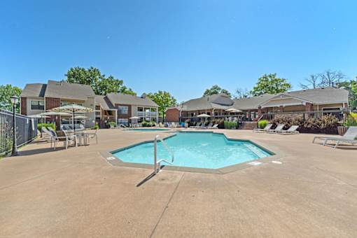 A large swimming pool surrounded by lounge chairs and umbrellas in a residential area.