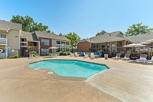 A swimming pool surrounded by lounge chairs and umbrellas in a sunny day.