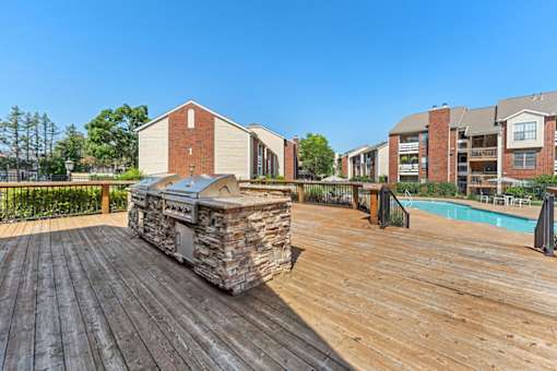 A wooden deck with a stone fireplace and a pool in the background.