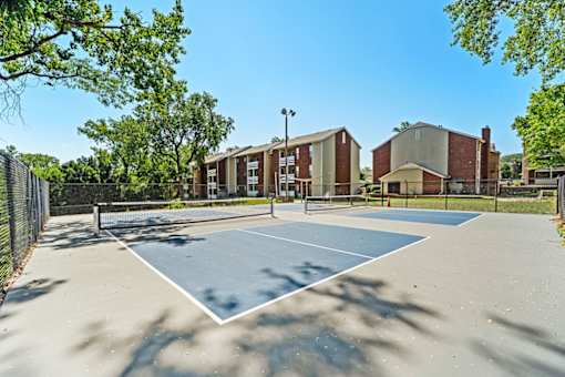 A tennis court is surrounded by a fence and a building.