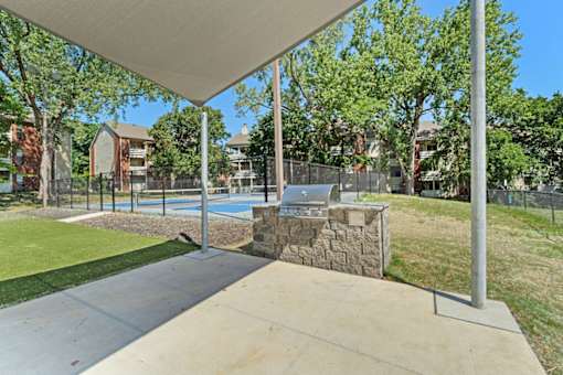 A pool under a white canopy with a stone wall and trees in the background.