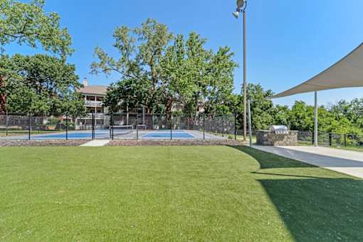 A green lawn with a tennis court and a house in the background.