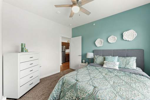 A bedroom with a bed, dresser, and ceiling fan.