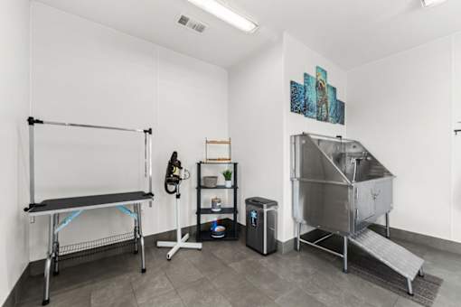 A room with a bench, a shelf, a trash bin, and a stainless steel container.