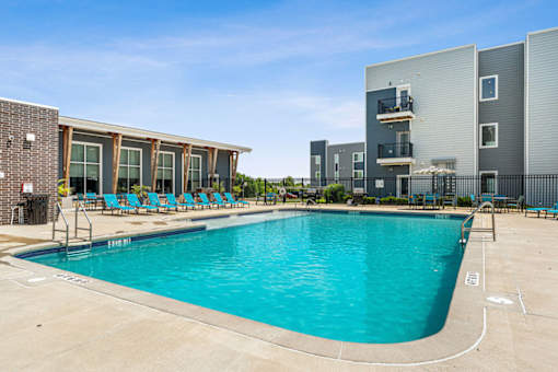 A swimming pool with blue water and lounge chairs in front of a building.