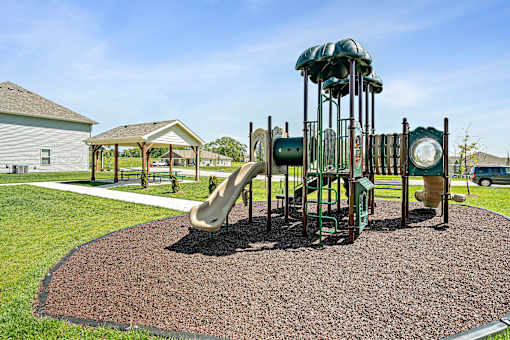 Three Bedroom Townhomes In Blue Springs, MO - Chapman Ridge Townhomes - A Playground Includes Multiple Slides, Soft Mulch Ground, Picnic Tables, Sidewalk Paths, And Green Lawn.