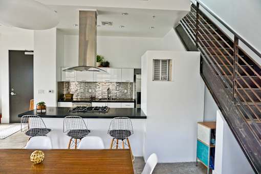 A modern kitchen with a black countertop and white chairs.