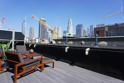 A wooden table and chairs are on a rooftop terrace with a city skyline in the background.