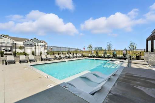 A large outdoor swimming pool with lounge chairs and a fence.