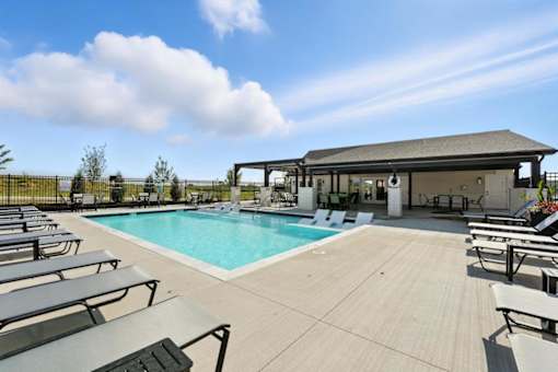 A pool with sun loungers and a pavilion in the background.