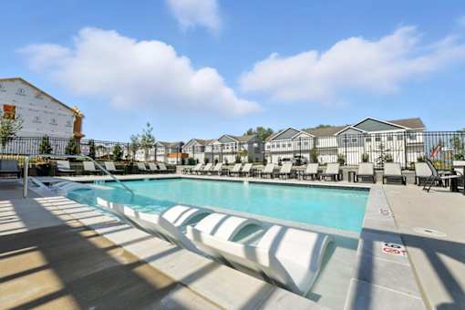 A large outdoor swimming pool with sun loungers and a building in the background.