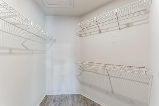 A white walk in closet with shelves and a wooden floor.