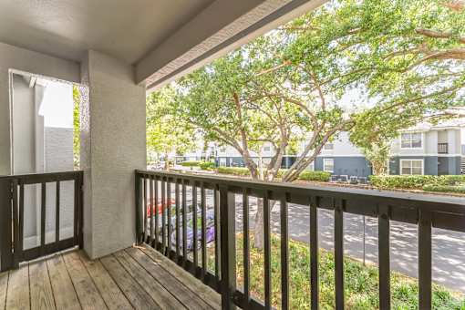 A balcony with a black railing and a view of a tree and a building.