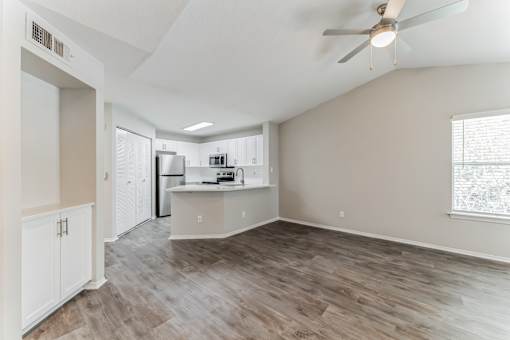 A spacious kitchen and living room with wood flooring and white walls.