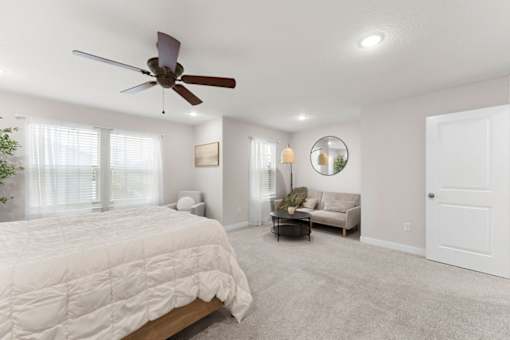 A bedroom with a bed, a couch, a ceiling fan, and a mirror.