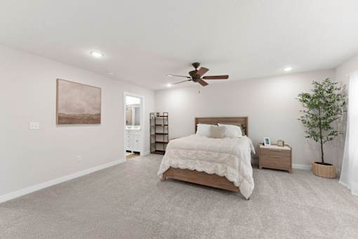 A bedroom with a large bed, a ceiling fan, and a painting on the wall.