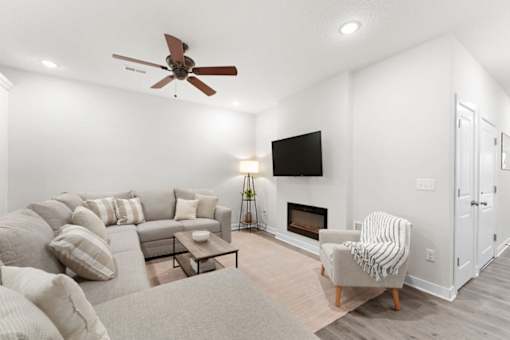 A living room with a grey couch, a coffee table, a fireplace, and a ceiling fan.