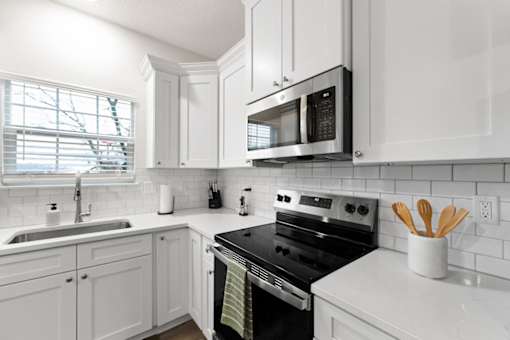 A white kitchen with a black stove and a black microwave.