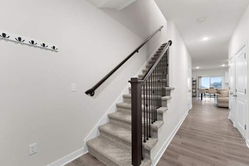 A staircase with a black railing and beige carpeted steps leads to a living room.