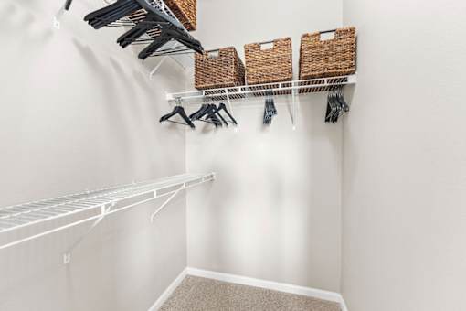 A white closet with clothes hanging and baskets on the shelf.