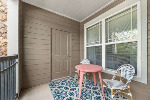 A small table and chair set is on a patterned rug on a porch.