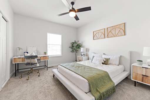 Dog-Friendly townhomes in Raymore, MO - Ascend - Spacious Bedroom With Large Bed, Nightstands With Lamps, Ceiling Fan, Plush Carpet, Work Desk, And Large Window.
