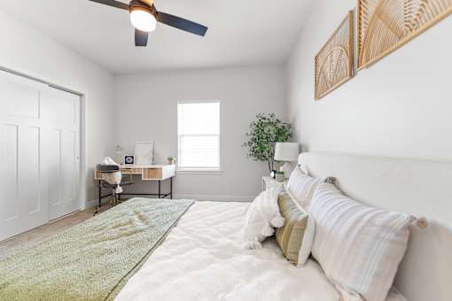 A bedroom with a bed, a desk, a ceiling fan, and a window.