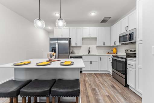 Three-Bedroom Townhomes in Raymore, MO - Ascend - Bright White Kitchen With Large Island Seating, Globe Pendant Lights, And Stainless Steel Appliances.