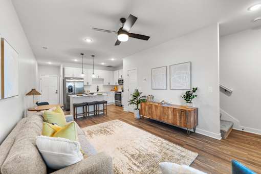 Townhomes for Rent in Raymore, MO - Ascend - Open Concept Living Room With Wood Style Flooring, Couch, Ceiling Fan, And View Of Kitchen.