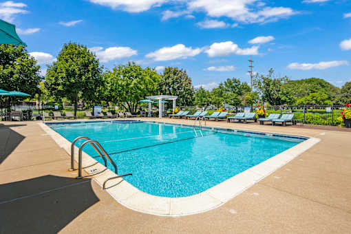A large outdoor swimming pool surrounded by trees and a clear blue sky.