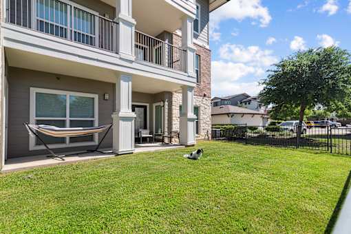 A dog is sitting on the grass in front of a two-story apartment building.