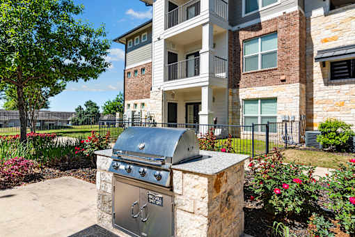A stone BBQ grill is in front of a building.