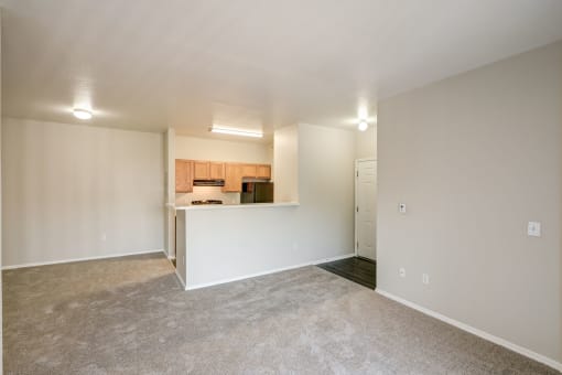 the living room and kitchen of an empty home with white walls and carpet