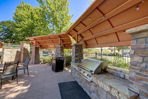 Aurora, CO, Pet-Friendly Apartments - Copper Flats - Well-Equipped BBQ And Picnic Area With Stainless Steel Grill, Arched Canopy, Dining Area, And Lush Greenery View.