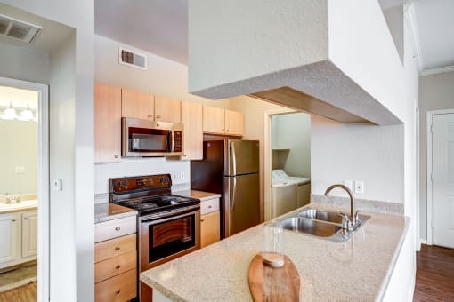 Apartments In Aurora, CO - Sonoma Resort At Saddle Rock - Kitchen With Granite-Style Countertops, Wood-Style Flooring, Light Cabinets, And Stainless-Steel Appliances.