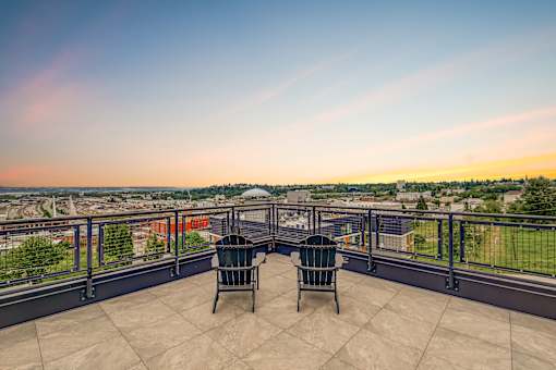 Two chairs are placed on a balcony overlooking a cityscape.