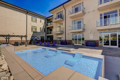 an apartment building with a pool and chairs in front of it