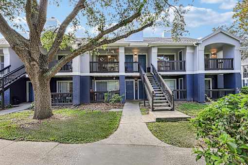 A tree in front of a two-story building with a balcony.