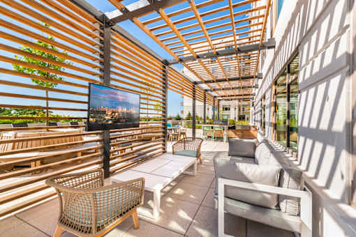 A patio with a white couch, a wicker chair, and a flat screen TV.