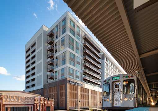 A train is on a track under a bridge next to a building.