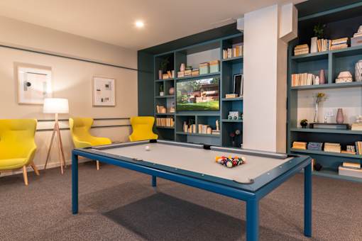 A pool table in a room with a yellow chair and a bookshelf.