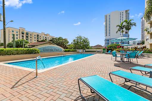 A pool with blue tiles and chairs in front of a hotel.