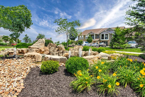 Riverstone - Landscaping with stone fountain, yellow flowers, trees, and shrubs