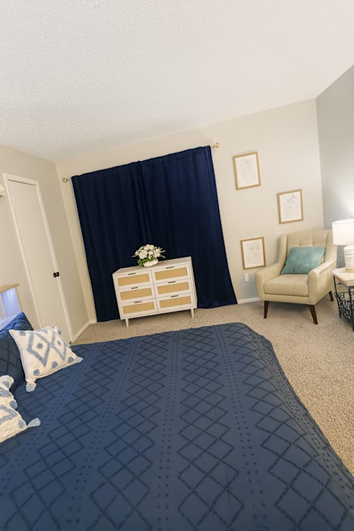 A bedroom with a bed, chair, and nightstand.