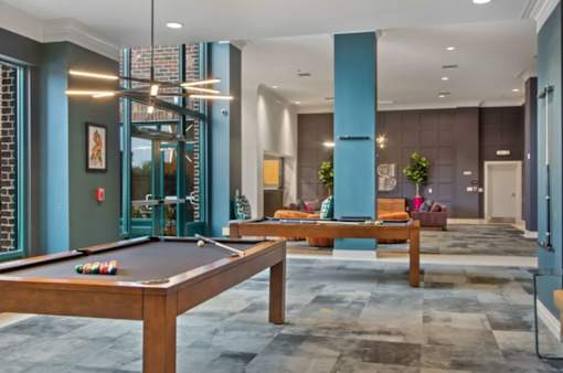 A pool table is in the middle of a room with a blue column and a couch.