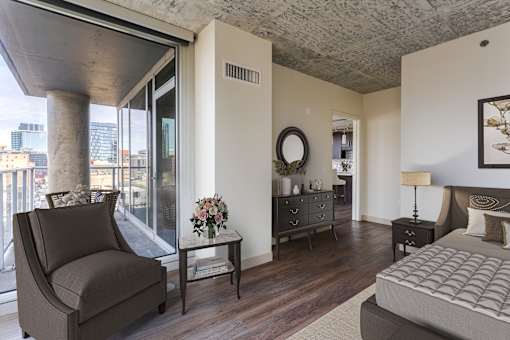 A bedroom with a large bed, a chair, and a table with a vase of flowers on it.