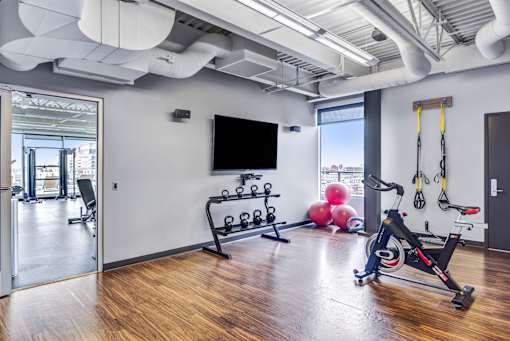 A gym room with a rowing machine, dumbbells, and a television.