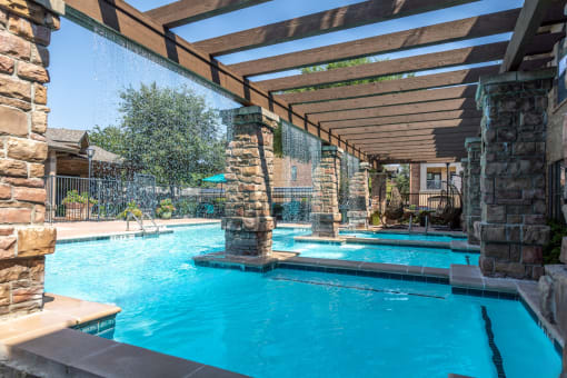 a resort style swimming pool with stone columns and a wooden canopy over it
