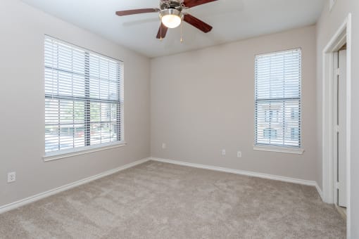 an empty bedroom with a ceiling fan and two windows